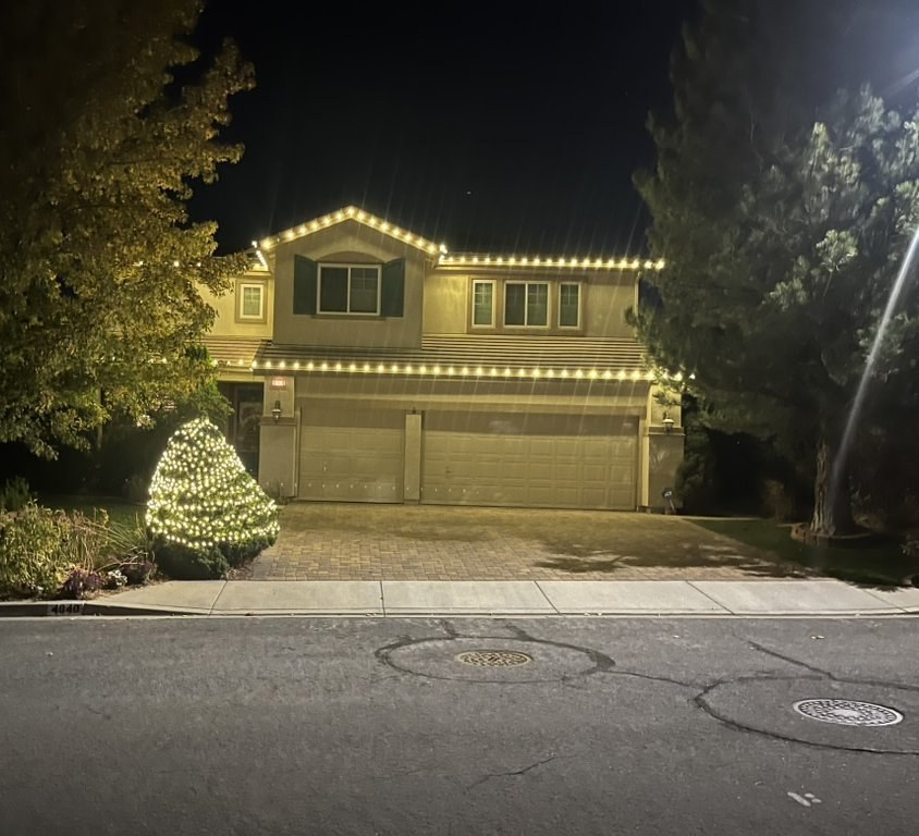 Two-story home with warm white roofline lights and a lit front tree